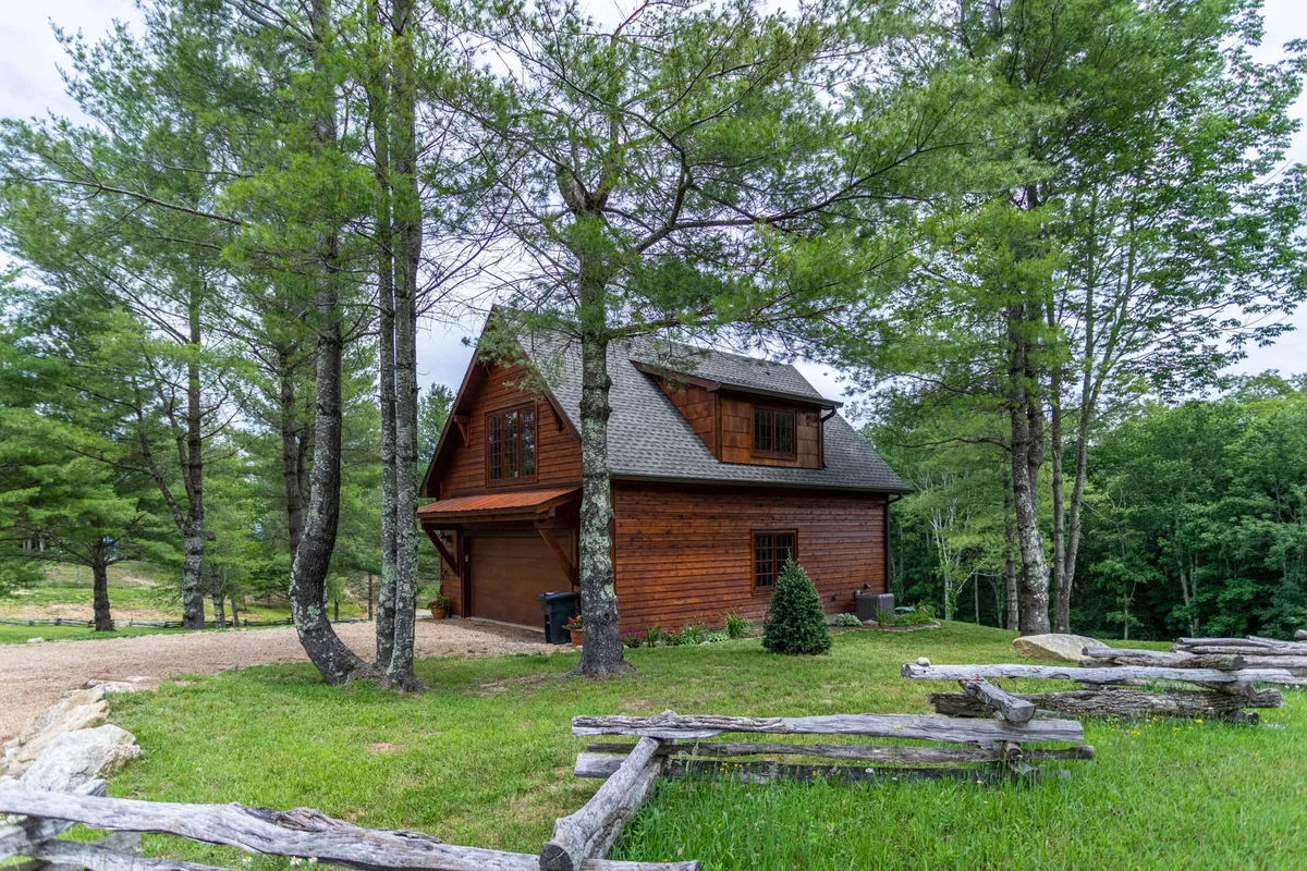 A charming wooden cabin nestled among tall trees, with a lush grassy lawn and a stone path leading to a cozy porch—perfect for catching sunset views. The peaceful setting invites guests to unwind and soak in the natural beauty of Banner Elk.