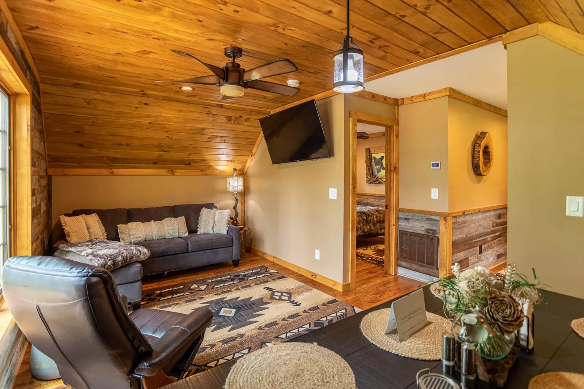 A comfortable living area featuring a plush sofa, area rug, pendant light, and a flat-screen television. The space is arranged for relaxation, offering a cozy spot to watch TV, read, or engage in conversation under soft, modern lighting.