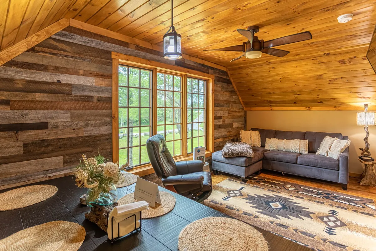 A spacious, comfortable seating area with large multi-pane windows, warm decorative lighting, and a wooden accent wall. The room is perfect for relaxing, socializing, and enjoying natural light and scenic views after a day of activities.