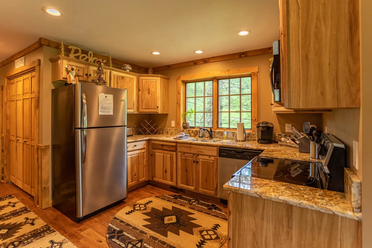 This image displays a cozy kitchen featuring granite countertops, rich wooden cabinets, and a window framing vibrant outdoor greenery. Decorative items add warmth, suggesting a lived-in, welcoming atmosphere ideal for family gatherings or peaceful coffee breaks.
