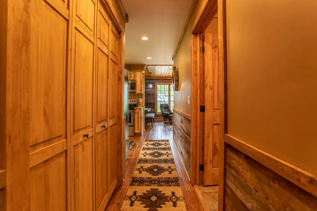 A cozy hallway showcasing rich wooden cabinetry, a textured runner rug, and doorways that invite guests to explore further into the home. The space exudes rustic charm and warmth, hinting at the inviting communal areas beyond.